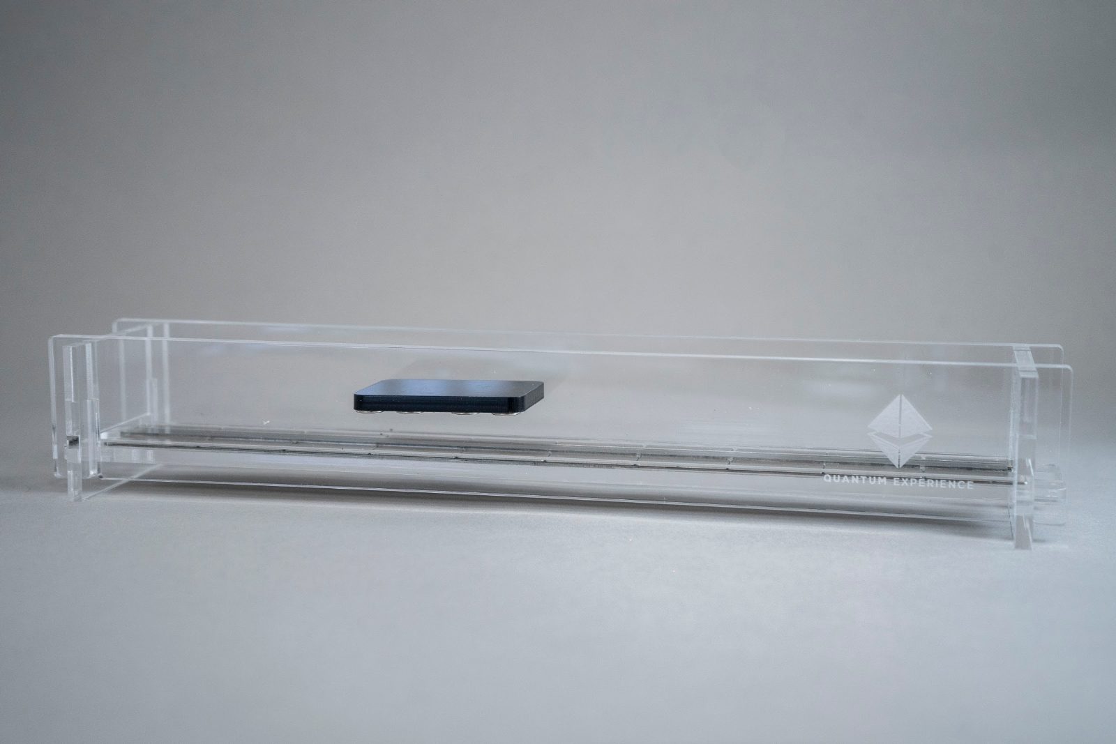 A small Perspex maglev train carriage floating a few millimetres above a magnet-lined track, seen at an angle