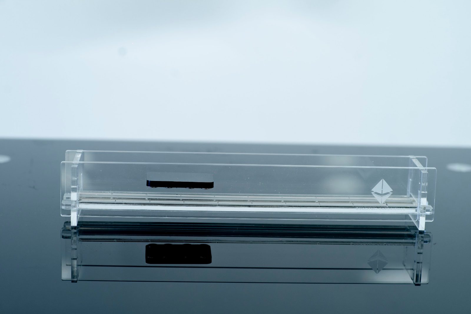 The maglev track on a dark reflective desk, the carriage floating above the rail with its reflection below