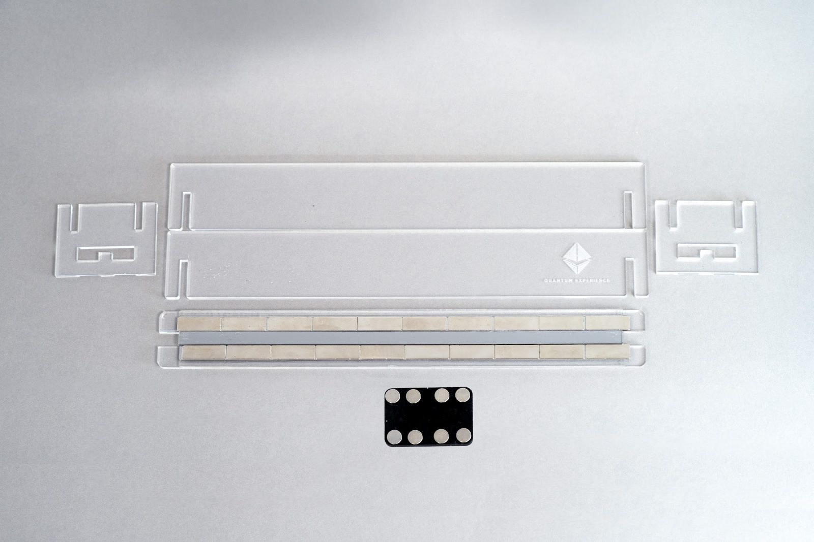 Flat lay of the project parts: Perspex track pieces and end caps, two rows of cube magnets, and a block of spare cube magnets